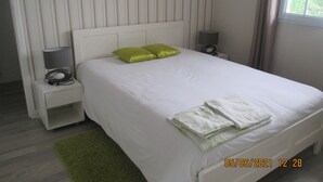 A neatly made bed with white bedding and two green pillows, a bedside lamp, and a small table with a lamp. - Basque country between sea and mountains, quiet ground floor apartment with garden  (ustaritz)