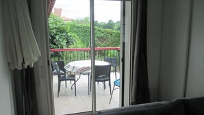 A balcony with a table and chairs, a sofa, and a view of greenery and buildings. - Basque country between sea and mountains, quiet ground floor apartment with garden  (ustaritz)