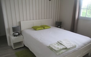 A neatly made bed with white bedding and two green pillows, a bedside lamp, and a small table with a lamp.