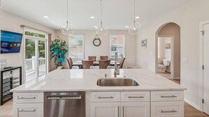 A spacious kitchen with a large island, modern pendant lights, and a dining area with a view to the outdoors. - Coastal Charm at Bayside, Golf Cart Access, Pools (Selbyville)