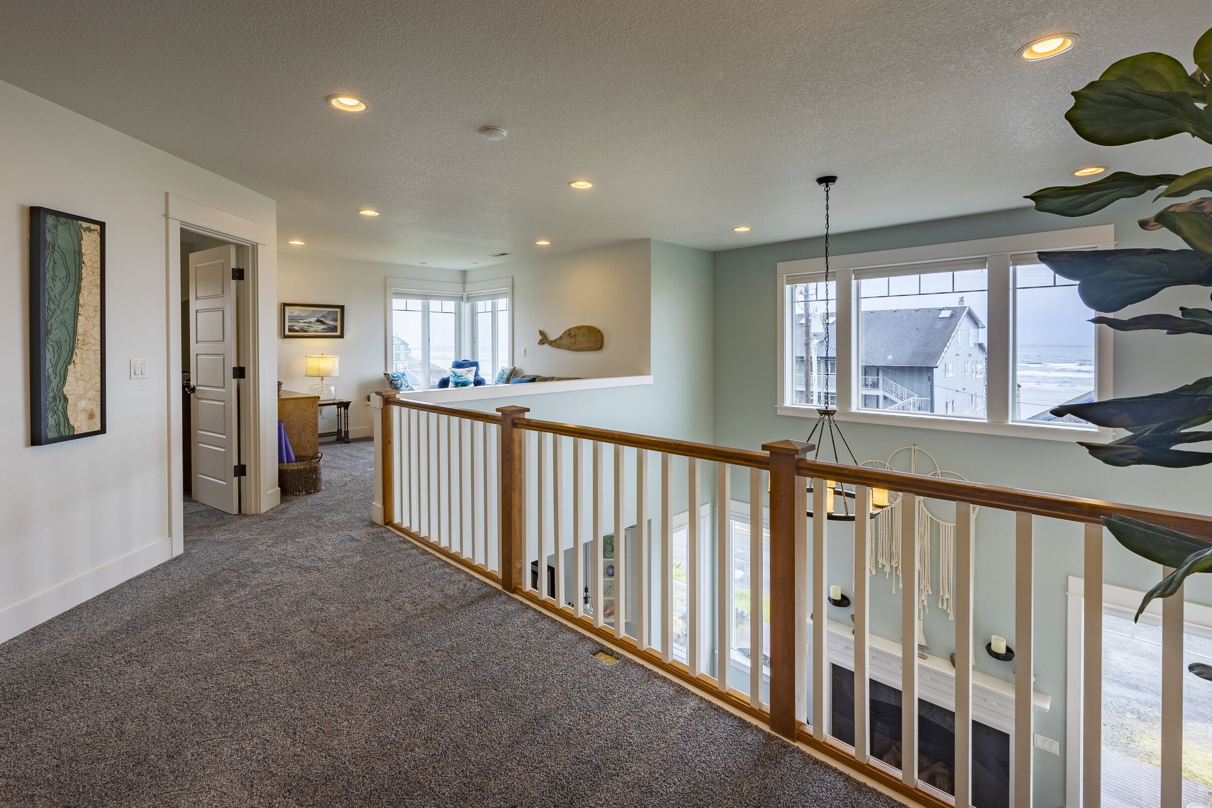 A spacious hallway with a carpeted floor, wooden railing, and a view of the ocean through large windows.