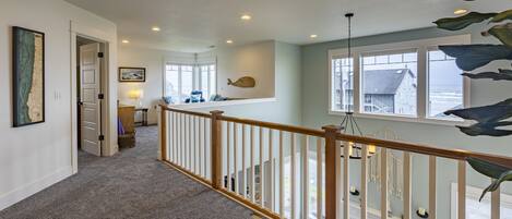 A spacious hallway with a carpeted floor, wooden railing, and a view of the ocean through large windows.