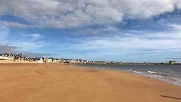 A wide sandy beach with a clear sky and scattered clouds.