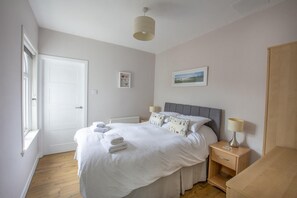 A bedroom with a bed, bedside tables, a window, and a door. - Helena Cottage (Leven)