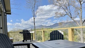 Une terrasse avec une table et des chaises, un barbecue et une vue sur les montagnes.