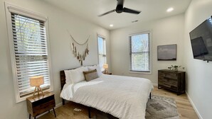 Une chambre à coucher avec un lit, un ventilateur de plafond, une télévision et une commode en bois.