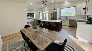 Une cuisine moderne dotée d’un îlot central, de meubles blancs et d’un coin repas avec une table et des chaises en bois.