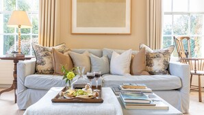 A living room with a light grey sofa, a wooden coffee table with books and a tray of cheese and grapes, and a large framed artwork on the wall. - Luxury Country Estate in West Cork (Bandon)