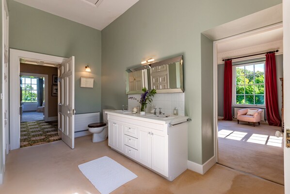 A bathroom with a white vanity, a large mirror, and a window with red curtains.