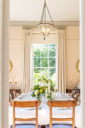 A dining room with a table set for two, a chandelier, and a window with curtains.