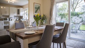 Un coin repas avec une table dressée pour quatre personnes, entourée de chaises, et une vue sur le jardin grâce à de grandes fenêtres.