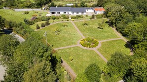 Un vaste domaine avec une grande pelouse centrale, entouré d’arbres et de quelques bâtiments.