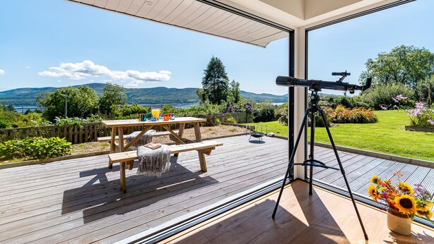 Une terrasse dotée d’un télescope, d’une table de pique-nique et offrant une vue sur un lac et des montagnes.
