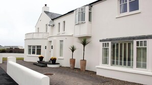 Une maison blanche à deux étages, dotée d’un balcon, de grandes fenêtres et de plantes en pot.