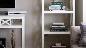Un salon avec un meuble de rangement blanc pour l’équipement audiovisuel, un téléviseur, une statue et une bibliothèque contenant des livres et une horloge.