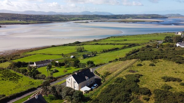 A coastal landscape with a house surrounded by green fields and a view of the sea. - Luxurious 5 bedroomed home with sea view close to beach (Lettermacaward)