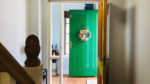 A green door with a wreath, a white wall, and a staircase leading to a room.