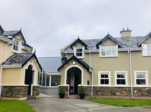 A two-story house with a stone facade, a central entrance with a black door, and a small garden area. - 3 bedroomed house minutes' walk from Kenmare town (Kenmare)