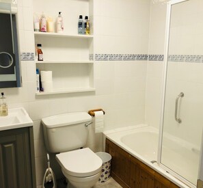 A bathroom with a toilet, a sink, a shower, and shelves with toiletries. - 3 bedroomed house minutes' walk from Kenmare town (Kenmare)