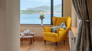 A room with a yellow armchair by a large window overlooking a body of water and hills. There's a small table with a teapot and cups, and a vase with flowers on the windowsill. - Luxury 4 bedroom holiday home overlooking the sea on Valentia Island (Farranreagh)