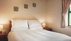 A neatly made bed with white linens, two bedside lamps, and three framed pictures on the wall.