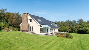 A modern house with a stone chimney, large windows, and a well-maintained lawn. - Stylish 4 bedroom home overlooking Kenmare Bay (Templenoe)