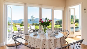 A round dining table with a polka dot tablecloth, white teacups, a white teapot, and a vase with pink flowers. - Stylish 4 bedroom home overlooking Kenmare Bay (Templenoe)