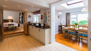 A spacious kitchen with a central island, wooden cabinets, and a dining area with a table and chairs. - Large house with adjoining cottage close to Waterville (Waterville)