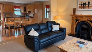 A cozy living room with a black leather sofa, wooden dining table, and a fireplace. - Holiday Home with view of Kenmare Bay Estuary (Kenmare)