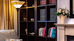 Un angolo lettura accogliente con una poltrona in pelle, una libreria piena di libri, una lampada decorativa e un vaso con fiori.