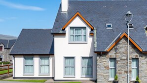 Une maison à deux étages, dotée d’une façade en pierre et d’un toit gris, avec de nombreuses fenêtres et une cheminée bien visible.