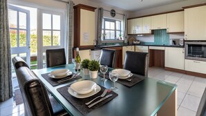 Un coin repas avec une table en verre, des chaises noires et une vue sur le jardin grâce à des portes ouvertes.