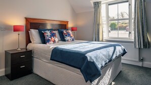 Une chambre à coucher bien rangée, avec un lit, deux tables de chevet, une fenêtre avec des rideaux et un radiateur.