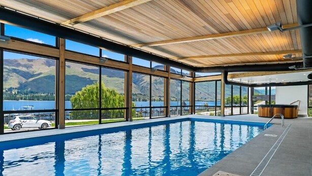 An indoor swimming pool with large windows offering views of a lake and mountains. - Central Wanaka Lakeside Condo (Wanaka)