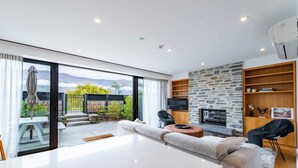A modern living room with a large sliding glass door leading to a patio, a fireplace, and a stone accent wall. - Central Wanaka Lakeside Condo (Wanaka)