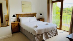 A bedroom with a bed, two bedside tables, a mirror, a painting on the wall, and a view of greenery through a sliding door. - Modern home with 3 bedrooms and 3 bathrooms in Kenmare town (Kenmare)