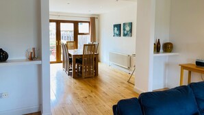 A modern living room with a blue sofa, wooden flooring, a dining area with a table and chairs, and a white radiator. - Modern home with 3 bedrooms and 3 bathrooms in Kenmare town (Kenmare)