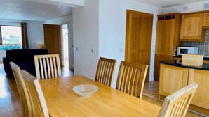 A modern dining area with a wooden table and chairs, a kitchen with wooden cabinets, and a view of the outdoors. - Modern home with 3 bedrooms and 3 bathrooms in Kenmare town (Kenmare)