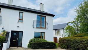 A two-story white house with a black door, a balcony with a metal railing, and a small garden area. - Modern home with 3 bedrooms and 3 bathrooms in Kenmare town (Kenmare)