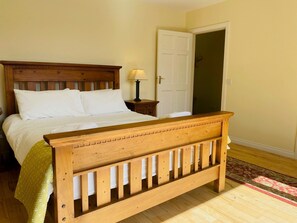 A bedroom with a wooden bed, a nightstand with a lamp, and a door to another room.