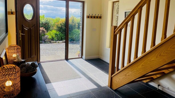 Un vestíbulo amplio con una escalera de madera, una puerta de cristal que da a un jardín y una pequeña mesa con adornos.