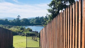 Une clôture en bois avec un portail qui mène à une zone herbeuse, et une étendue d’eau en arrière-plan.