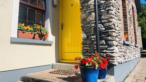 Une porte jaune portant le numéro 8, un mur de pierre et des plantes en pot sur le rebord de la fenêtre.