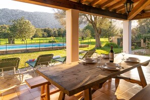 A wooden table set for dining with a view of a swimming pool and mountains in the background. - Villa Can Pontico la Vall By SunVillas Mallorca (Pollença)