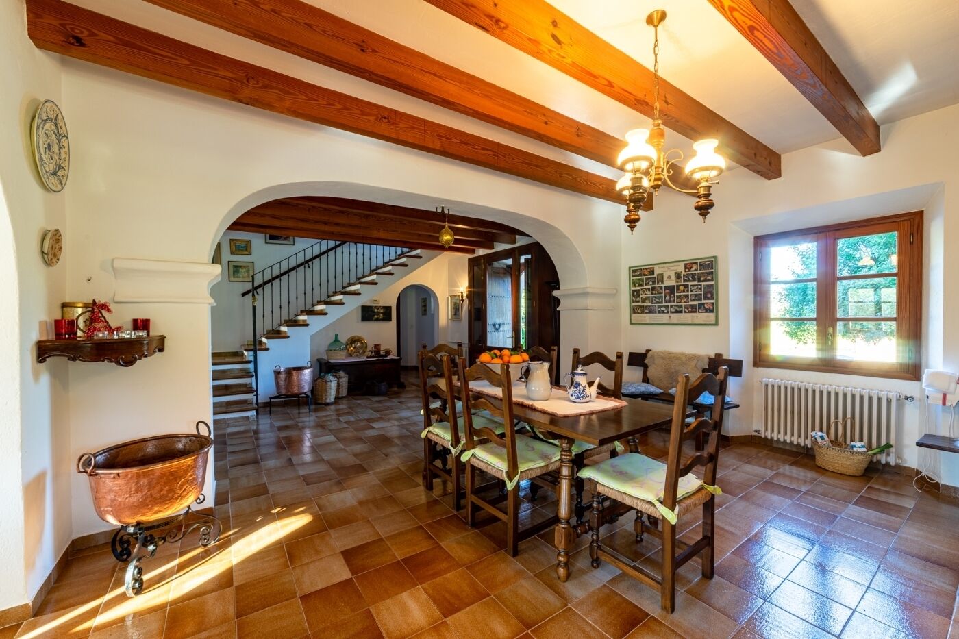 Zona pranzo con tavolo in legno, sedie e un lampadario. Una scala conduce a un'altra stanza.