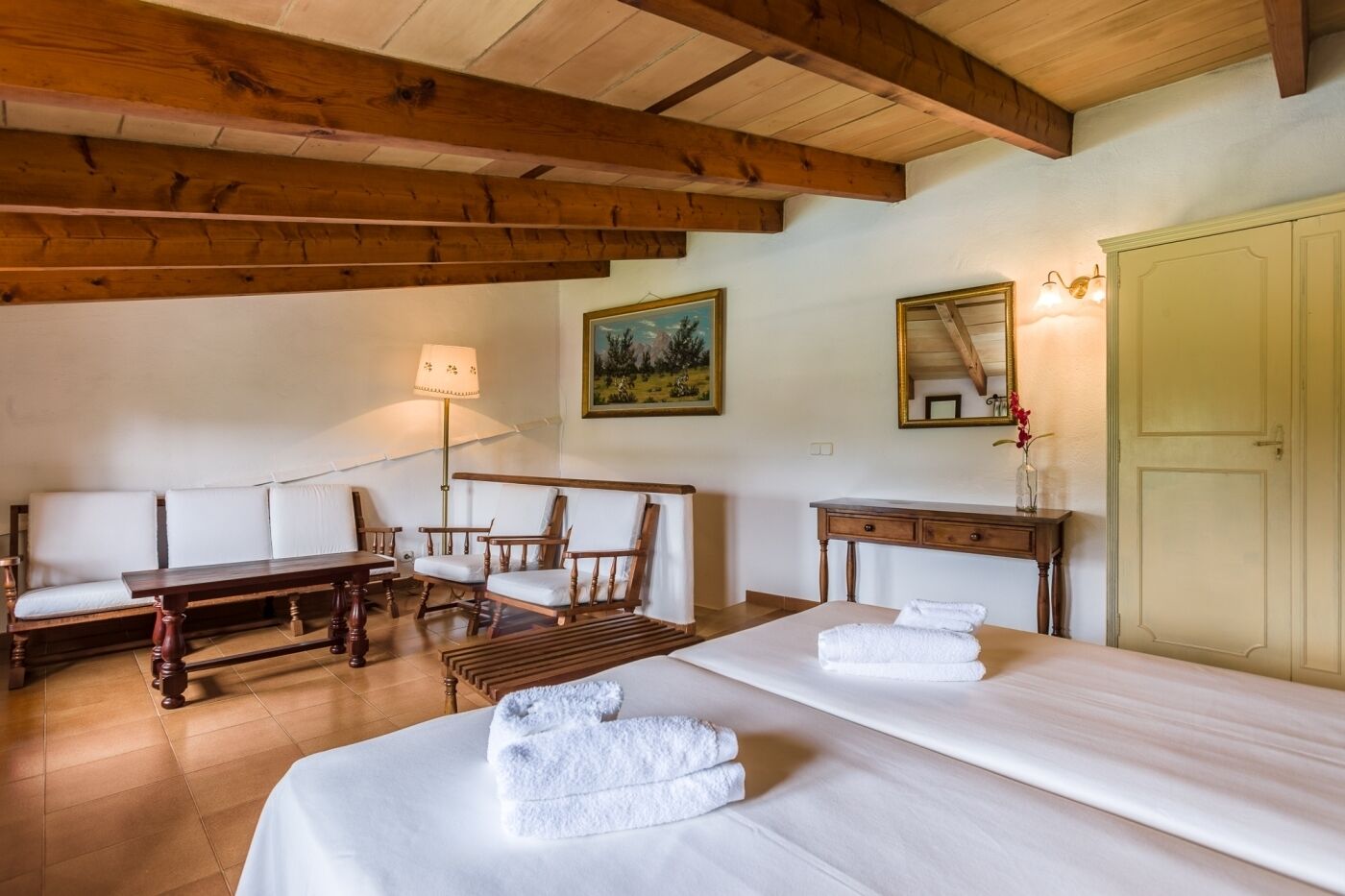 A hotel room with two beds, a sofa, a wooden table, a desk, a lamp, and a painting on the wall.