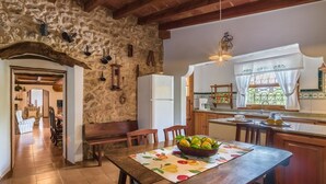 A rustic kitchen with stone walls, wooden beams, and a dining area with a table set for two. - Villa Can Mart By SunVillas Mallorca (Pollença)