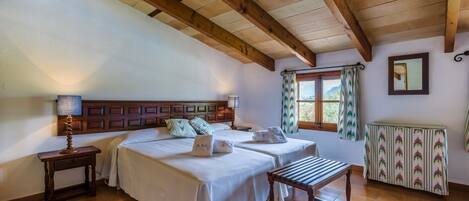 Un dormitorio con dos camas, cabeceros de madera, mesitas de noche con lámparas, una ventana con cortinas y un radiador.