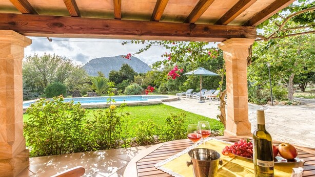 A covered outdoor area with a pool, a table with a bottle of wine, and a bowl of grapes. - Villa Can Mart By SunVillas Mallorca (Pollença)