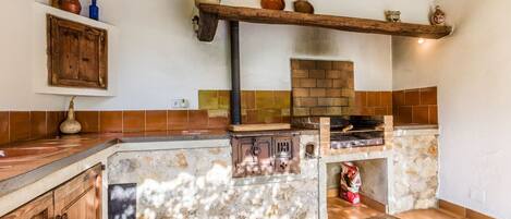 A rustic kitchen with a brick oven, wooden cabinets, and a stone island.